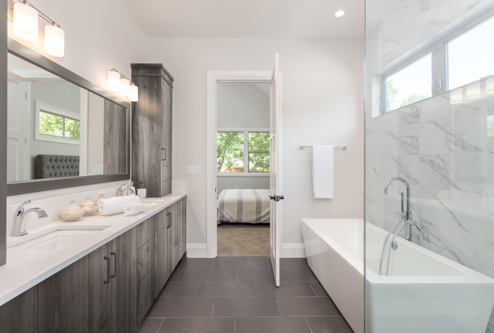 master bathroom interior in luxury home large mirror, shower, and bathtub. Includes dark hardwood cabinets and tile floor. View of bedroom